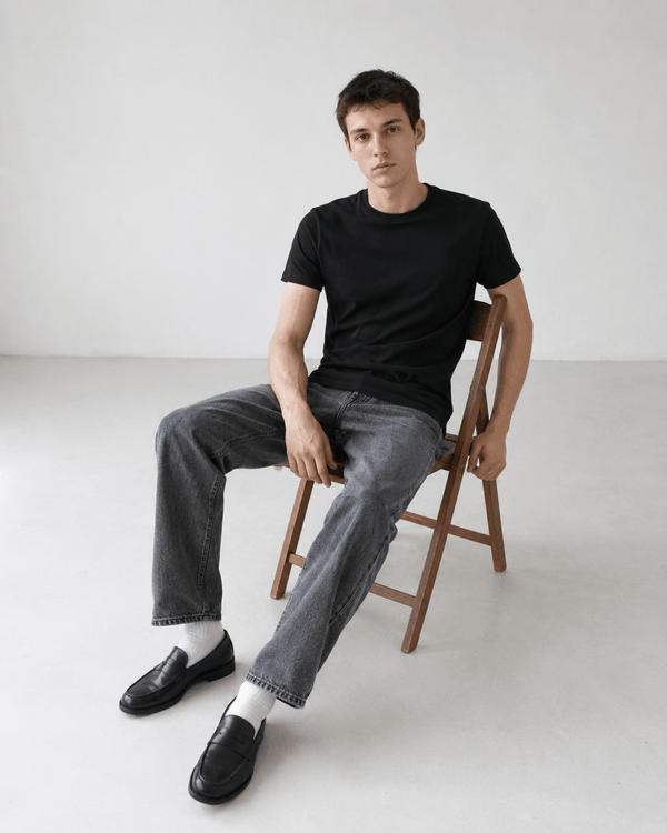 Homme mince en t-shirt noir assis sur une chaise